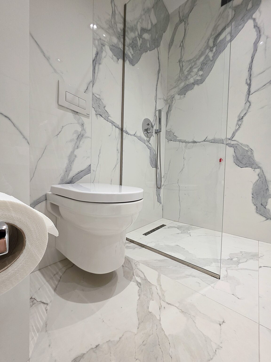 Wall-hung toilet and walk-in shower with chrome hand shower in the marble-effect bathroom