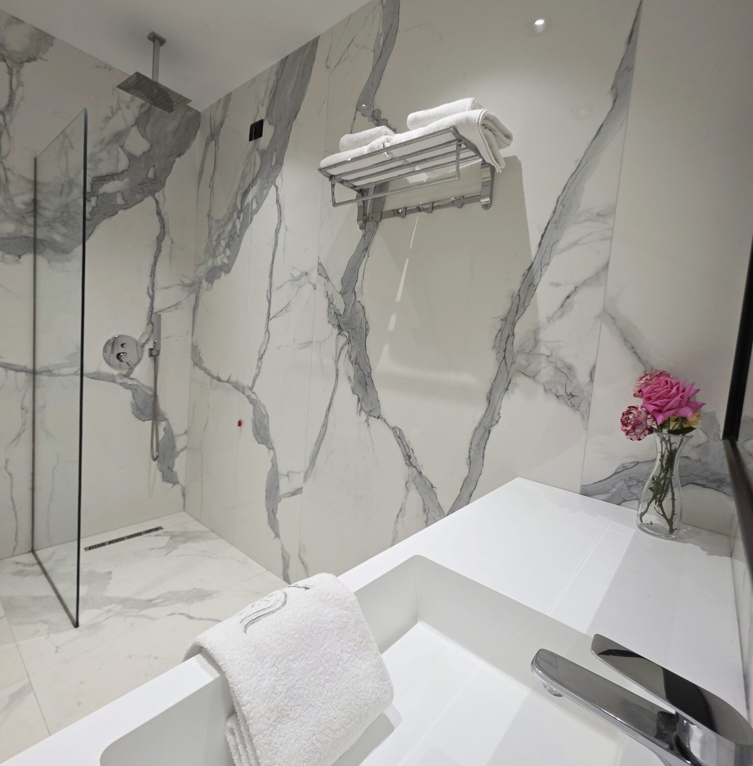 Walk-in shower, marble-effect walls and roses beside the basin in the Valza Suite bathroom