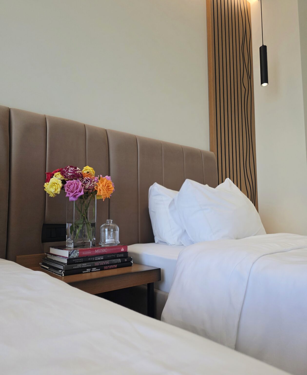 Colourful roses, a glass candle holder and books on the bedside shelf between the two beds