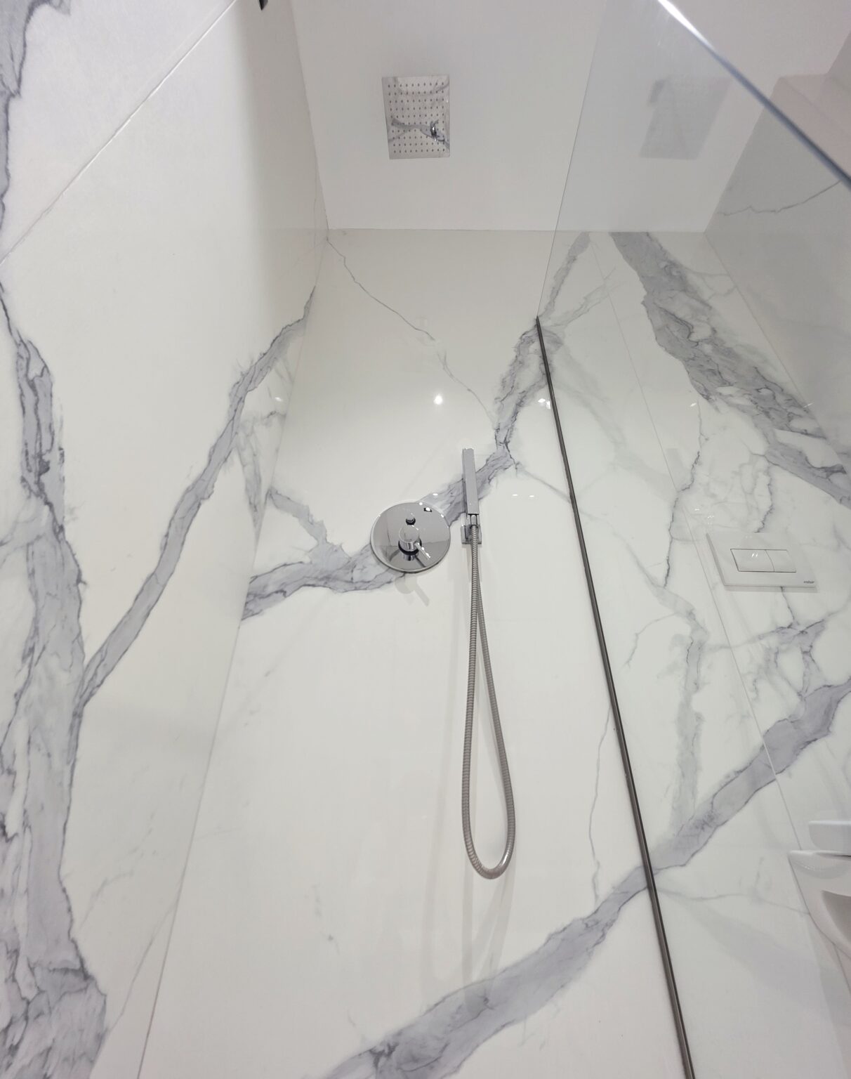 Close-up of the chrome shower mixer and hand shower hose against marble-effect walls