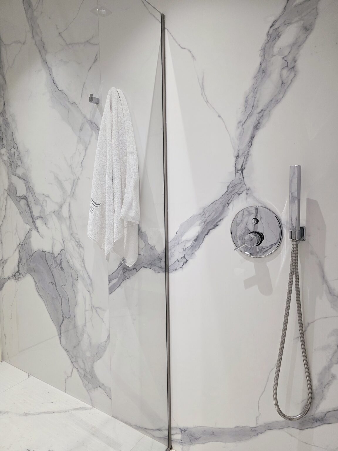 Shower with marble-effect walls, glass screen, chrome mixer, hand shower and a hanging white towel