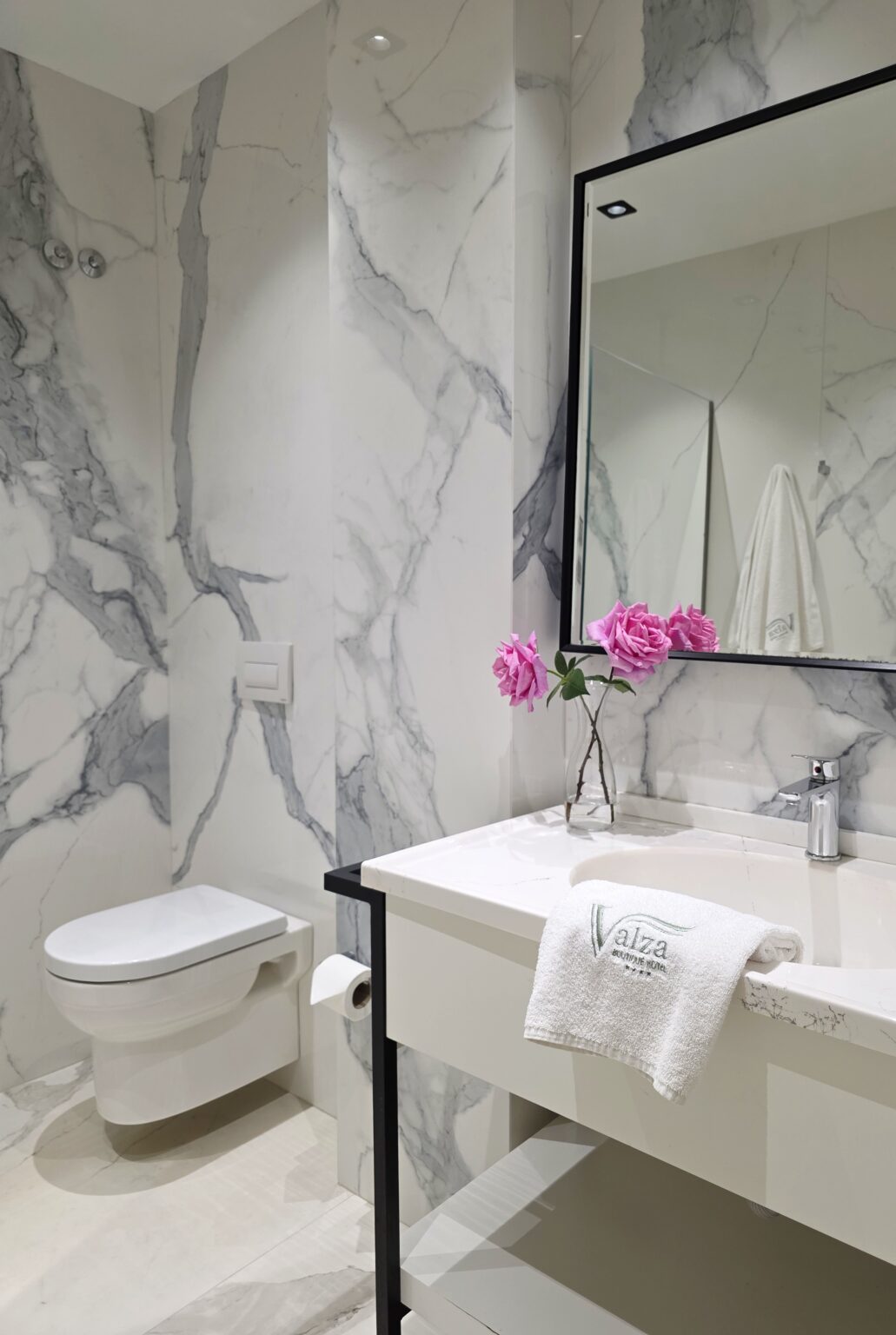 Double Superior bathroom with white marble-effect walls, basin, black-framed mirror and pink roses