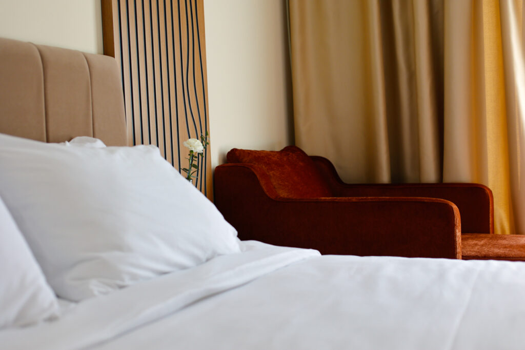 White pillows on the king-size bed with a rust velvet sofa and gold curtains behind