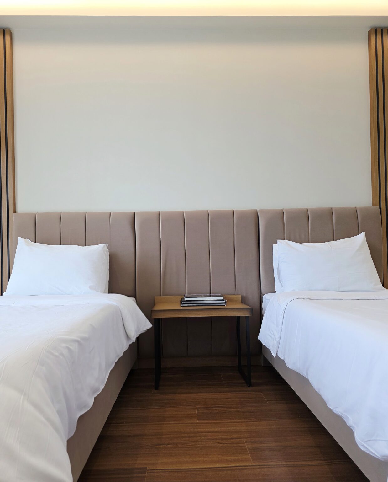 Two single beds of the Twin Deluxe Room seen head-on under a tall beige padded headboard