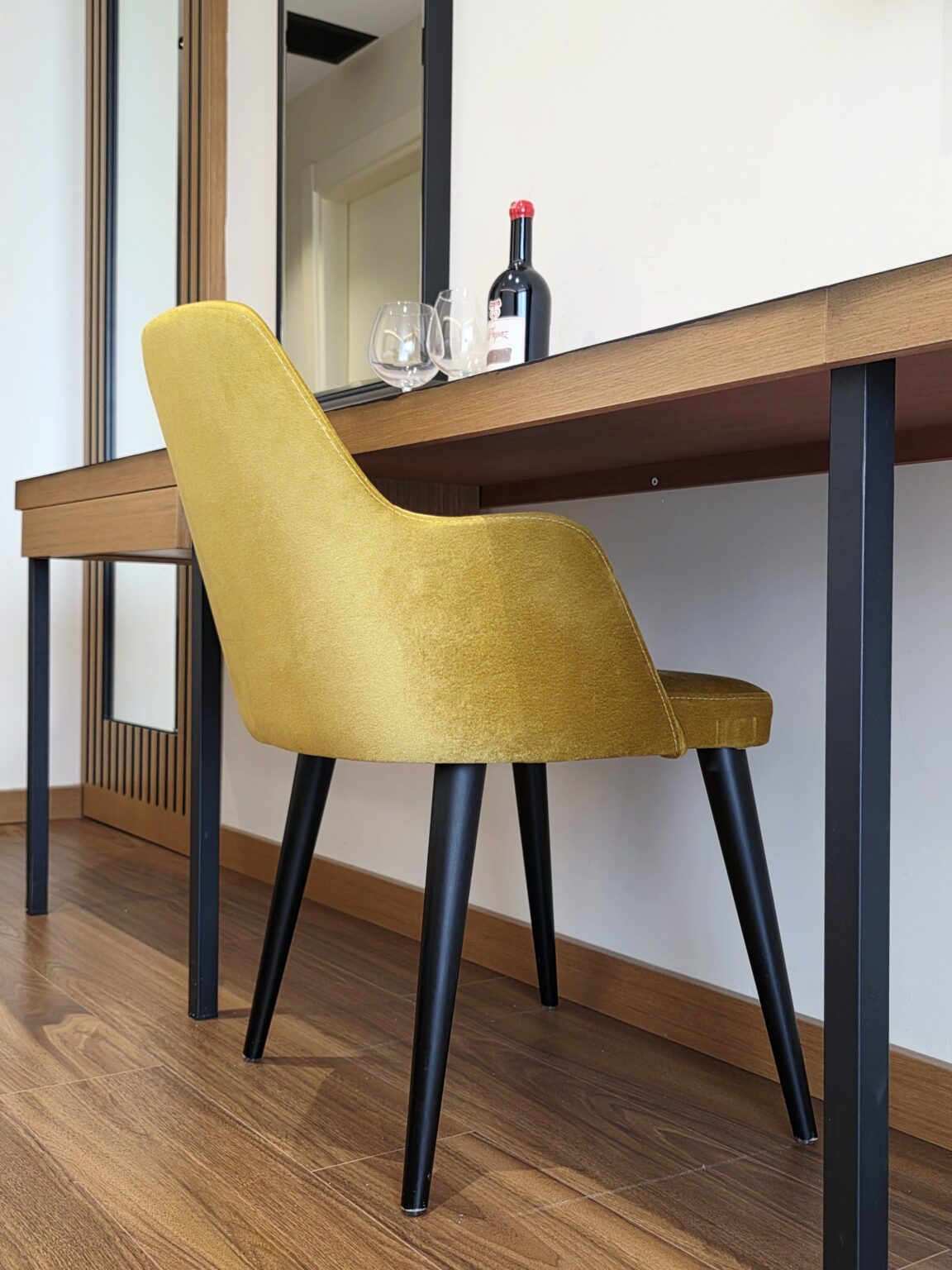 Close-up of the mustard-yellow velvet chair with black legs tucked under the wooden desk