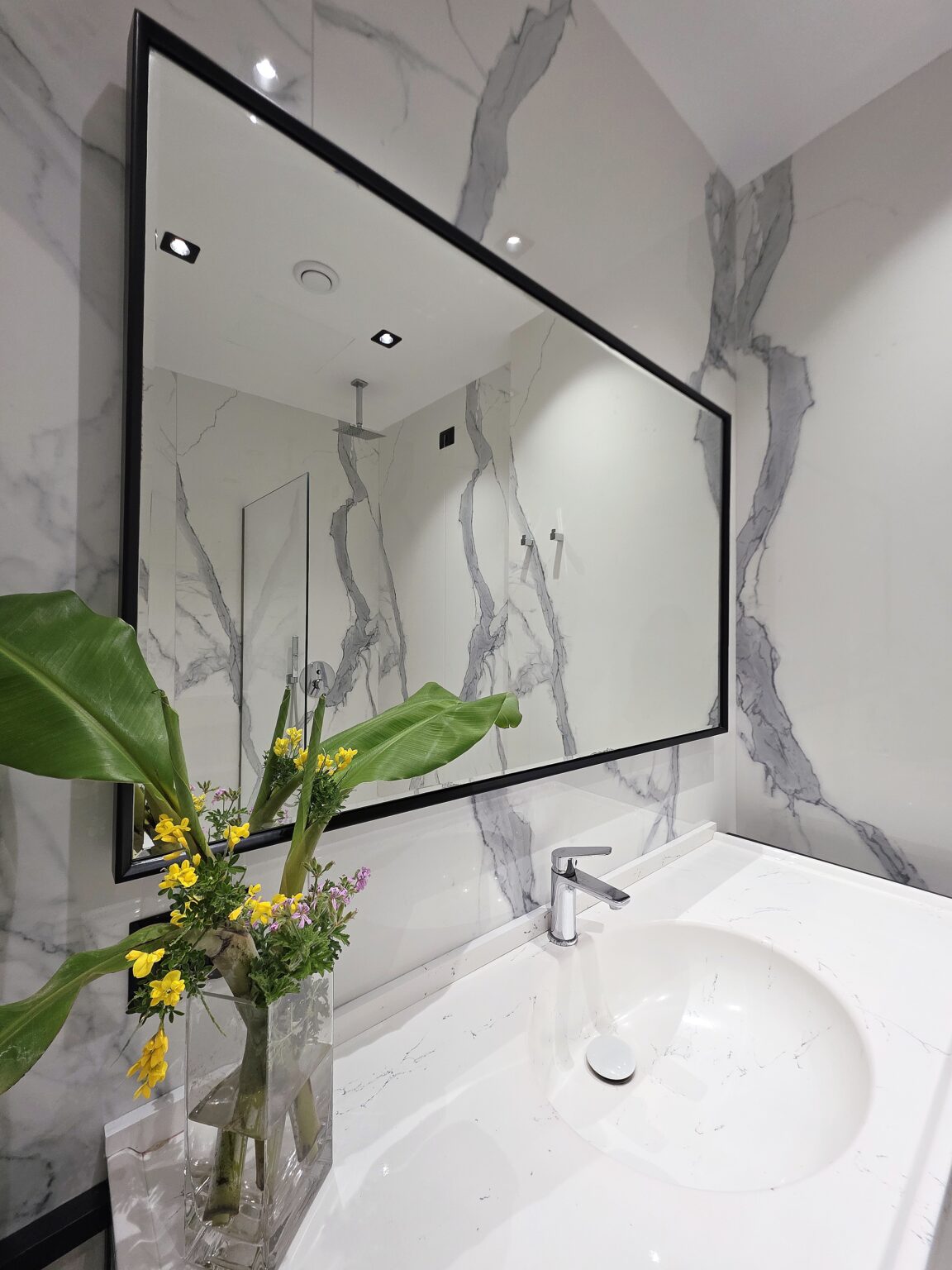 Bathroom with marble-effect walls and a black-framed mirror reflecting the walk-in rain shower