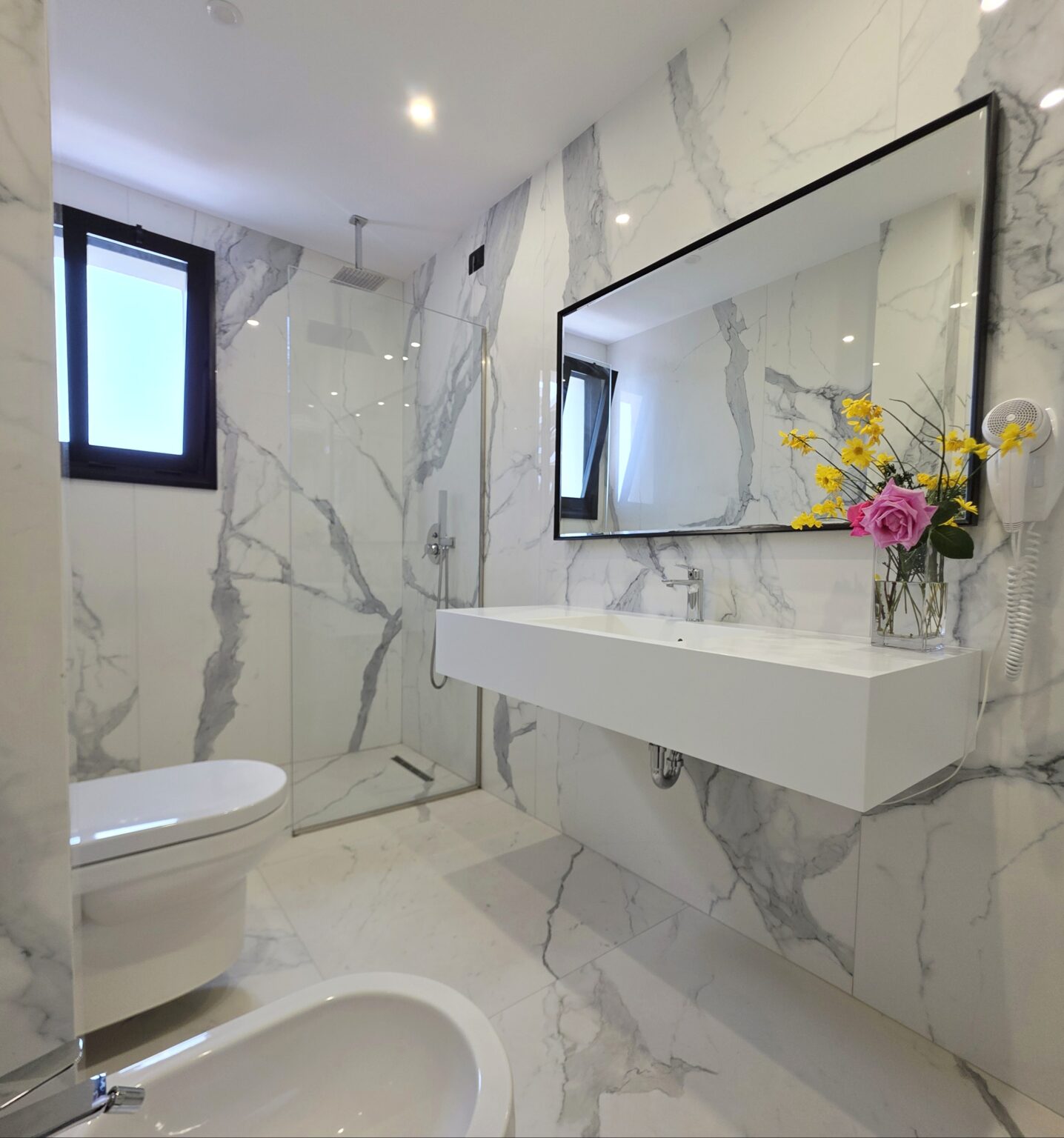 Suite bathroom in white marble-effect tiles with a walk-in glass shower, floating basin and large mirror