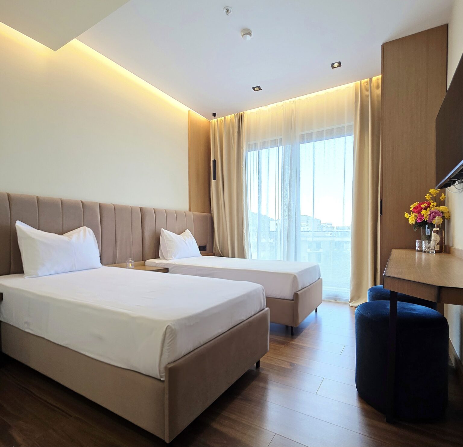 Children's bedroom of the Family Suite with two single beds, a floor-to-ceiling window and navy pouffes under a desk