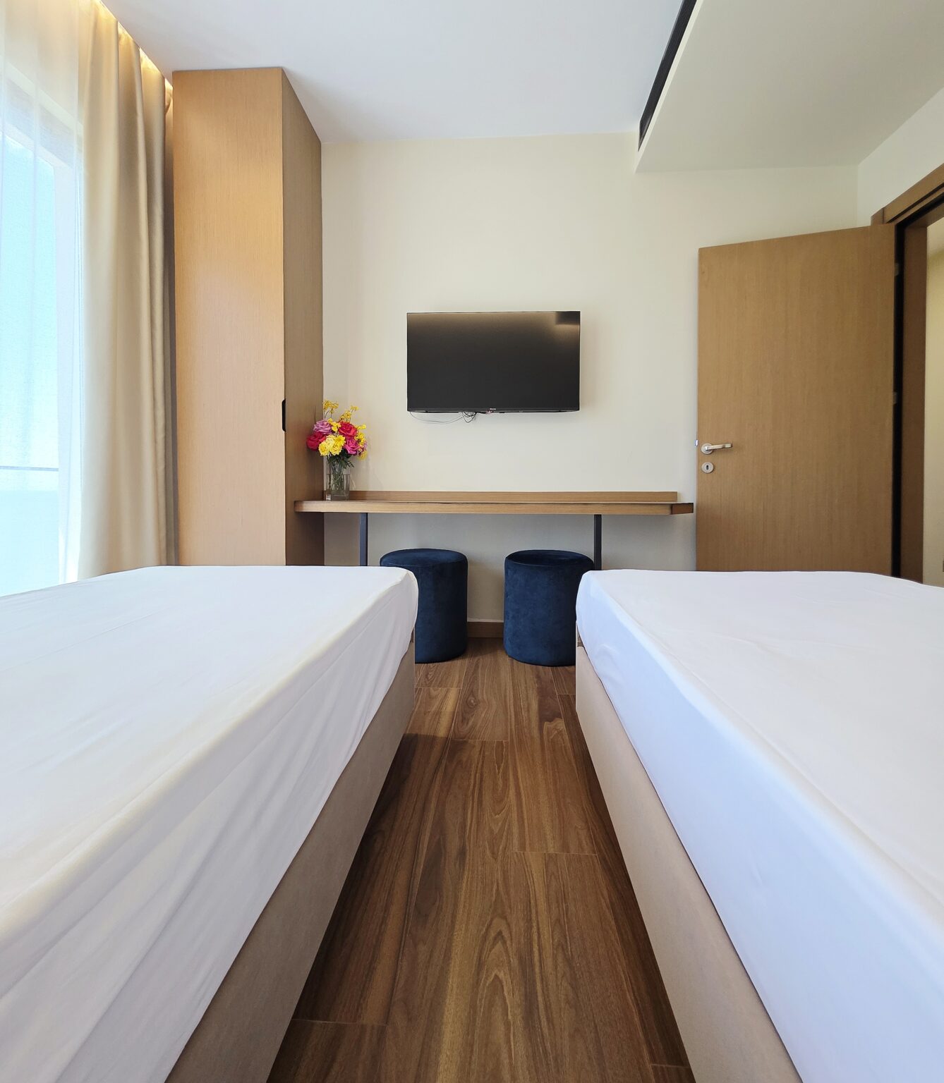 Children's room seen from the foot of the twin beds, with wall-mounted TV, floating desk and navy pouffes