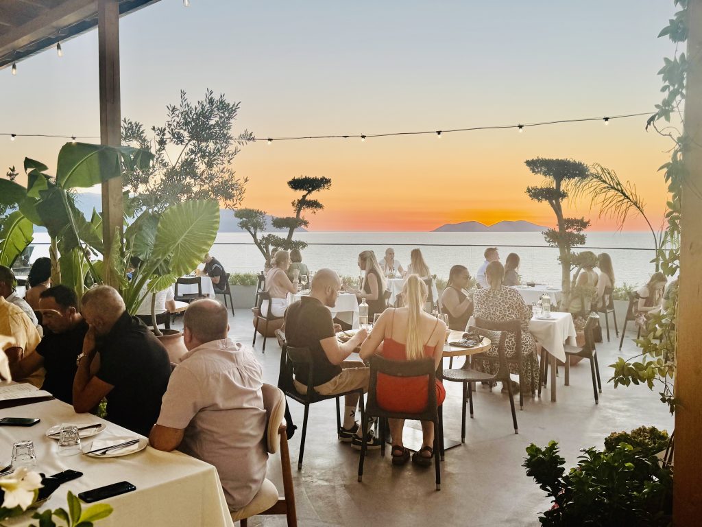 Eden_4 Eden by Valza rooftop terrace full of diners at sunset, with string lights, plants and the sea beyond